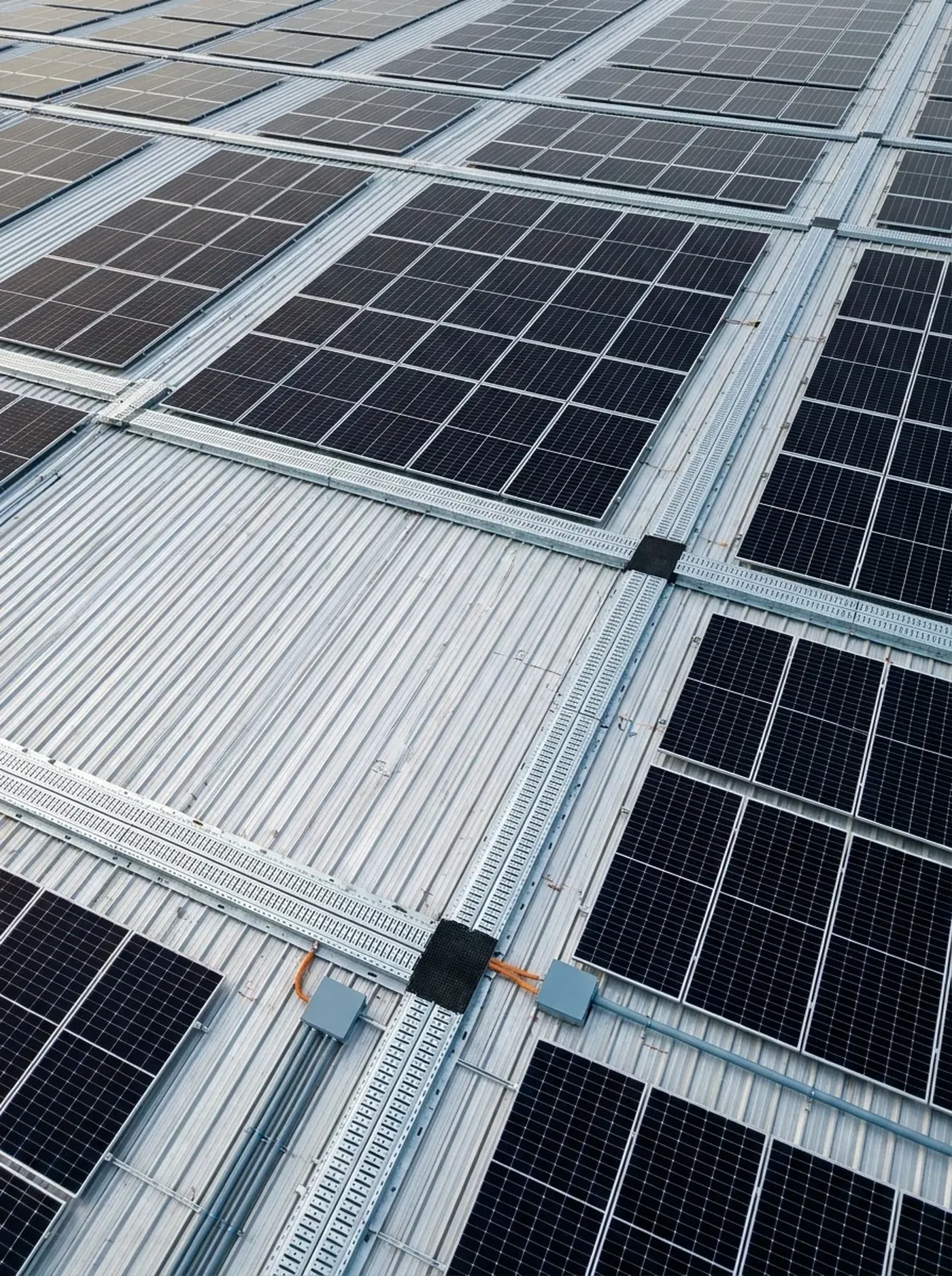 Vista cenital de una cubierta metálica con filas de paneles solares y pasillos técnicos entre ellas